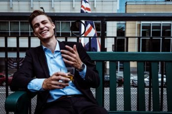 expats-from-uk.jpg expats from UK: Young man in a suit relaxes on an outdoor patio with a beer and a British flag in the background