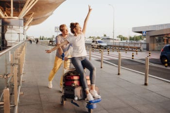 Two people playfully ride a luggage cart at the airport, enjoying the peace of mind provided by annual travel insurance.