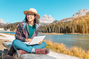Happy Asian woman working on laptop on mountain lake background in autumn. The concept of remote work and freelancer patriot exchange