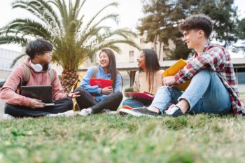 Group of multiracial international exchange university student friends sitting on the grass in the college campus geoblue navigator for students, crew members, and missionaries