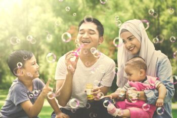 insurance-for-indonesian-citizens A happy Indonesian family blowing bubbles outside, feeling safe knowing they are protected by insurance for Indonesian citizens