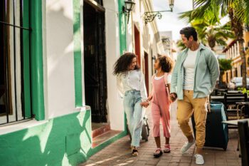 Tourist family A mother, father, and young daughter walking together and pulling suitcases, having secured overseas medical insurance before traveling abroad.