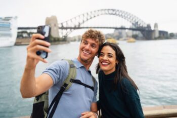 couple-by-sydney-harbour-bridge A happy couple taking a selfie in front of Sydney Harbour Bridge, having bought travel insurance for Australia