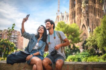 couple-in-barcelona-spain a happy couple taking a selfie in front of the Sagrada Familia in Barcelona, having purchased travel insurance for Spain