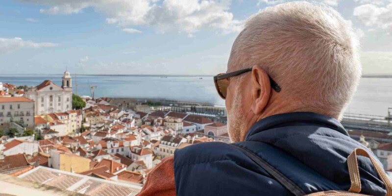 a mature man visiting Lisbon, Portugal, looking out at the old town view, indicating the importance of buying travel insurance for Portugal