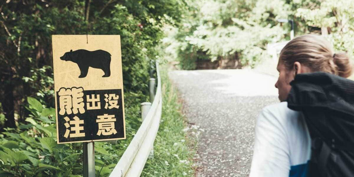 bear-sign-japan A tourist walking past a bear warning sign in a rural area of Japan, highlighting the important of buying robust travel insurance for Japan