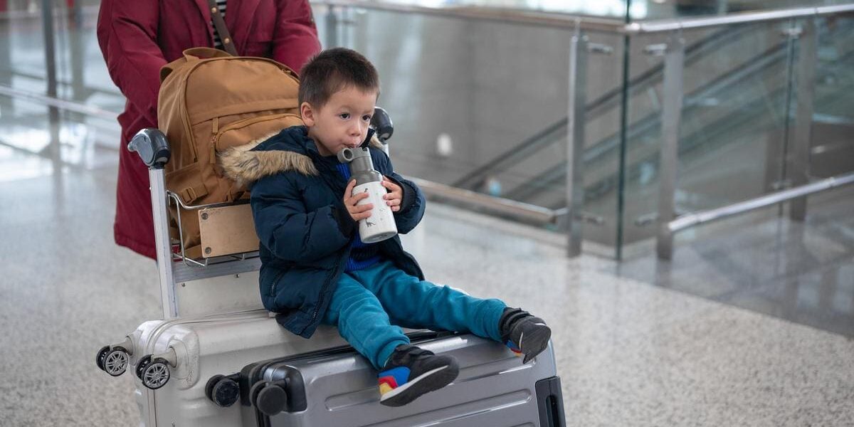 child-drinking-in-airport a toddler drinking from a reusable water bottle while sitting on a suitcase trolley, one of many great holiday travel tips