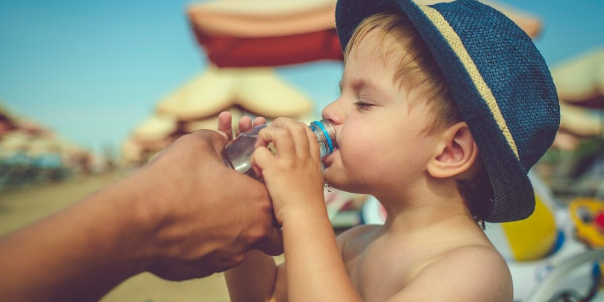 child-drinking-water A child drinking water from a bottle on a beach during a hot day, illustrating the importance of staying hydrated and following safety tips, like buying travel insurance for Spain