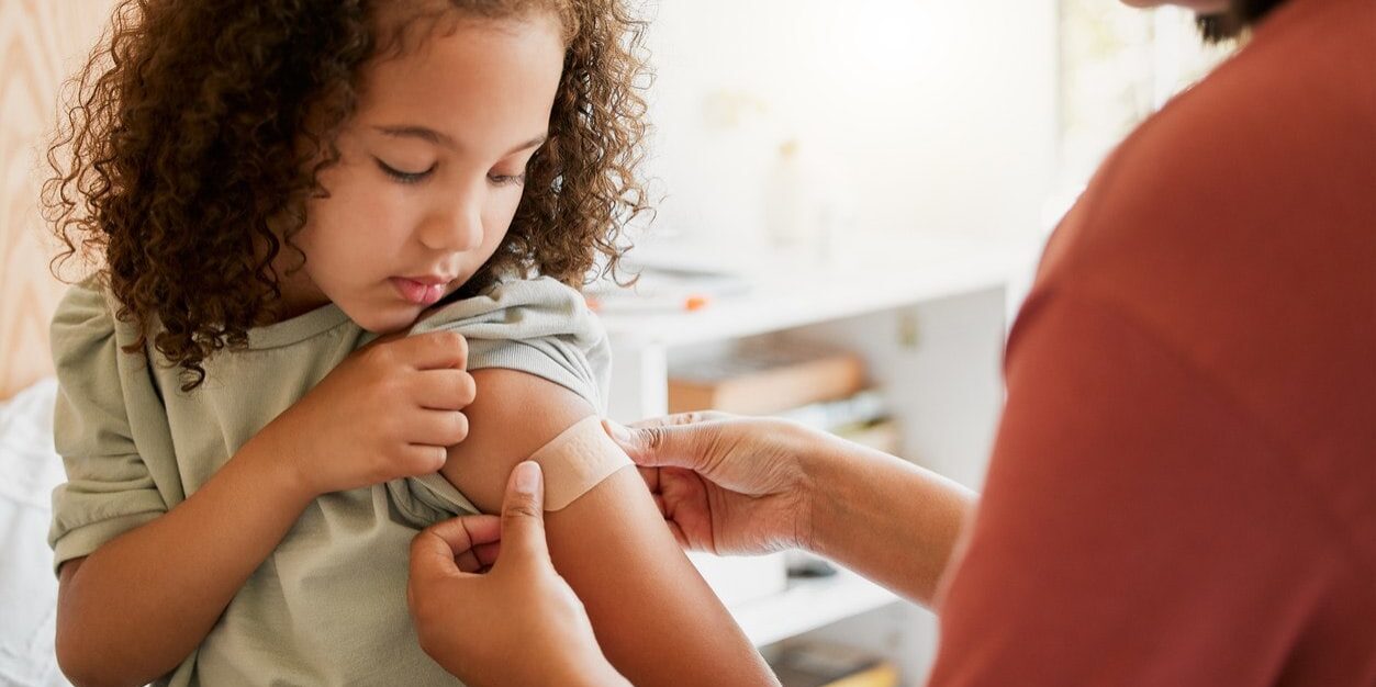 child-vaccination A doctor applying a plaster on a little girl after giving her a vaccination, as part of the children’s program for healthcare