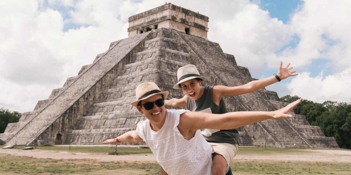 couple-in-mexico a happy couple posing in front of a pyramid in Mexico, where tourists are advised to buy travel insurance for Mexico