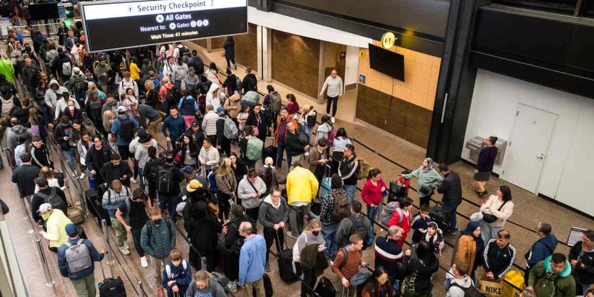 crowded-airport-usa A crowded airport security area in the United States, with passengers lined up in long queues with their luggage.