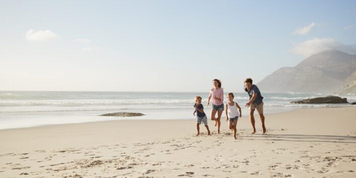 Parents Running Along Beach With Children On Summer Vacation expat travel health insurance for individuals and families
