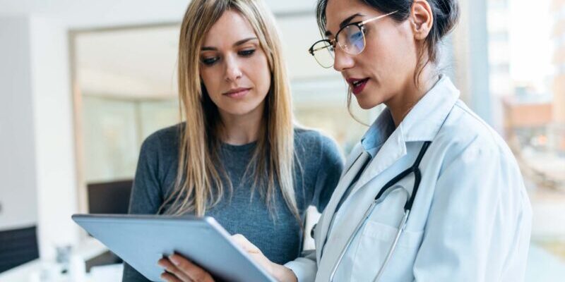 healthcare-costs-in-the-us a female patient talking to a doctor and looking at a clipboard