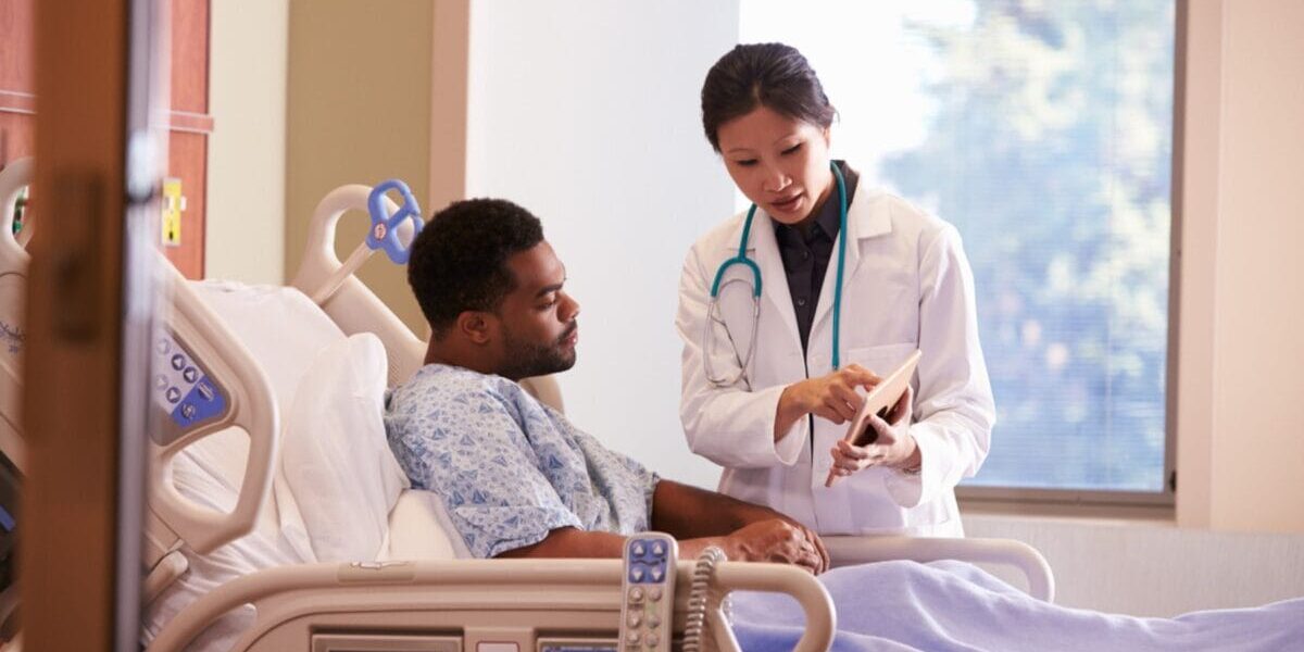 hospital-patient-in-bed a male patient laying in a hospital bed talking to a female doctor, reflecting on the importance of having Schengen visa insurance when visiting Europe