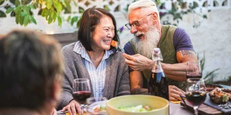 Happy senior people having fun at barbecue dinner - Multiracial mature friends eating at bbq meal - Food, friendship, relationship and summer lifestyle concept - Focus on asian woman face Australian mature couple homecoming barbecue