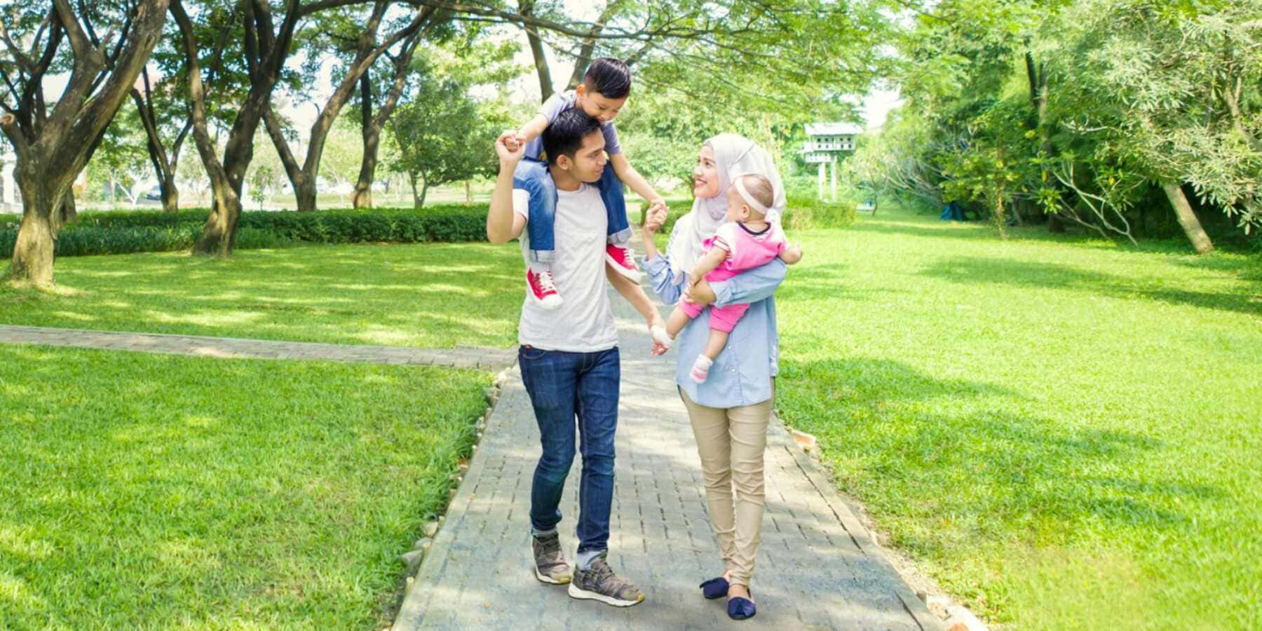 indonesian-family-walking-in-park a happy Indonesian couple walking along a footpath in a lush green park carrying their two small children