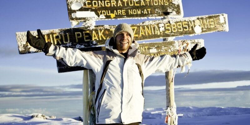 Climber at the Top of Mount Kilimanjaro a man standing at the top of Mount Kilimanjaro, highlighting the importance of securing medical evacuation insurance when visiting remote locations
