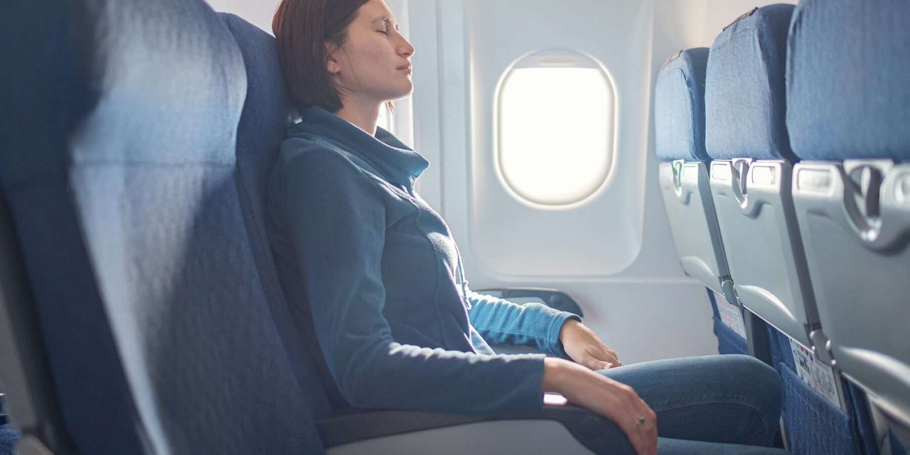 nervous-passenger a female passenger sitting with her eyes closed in a window seat on a plane, hoping she is flying with one of the safest airlines