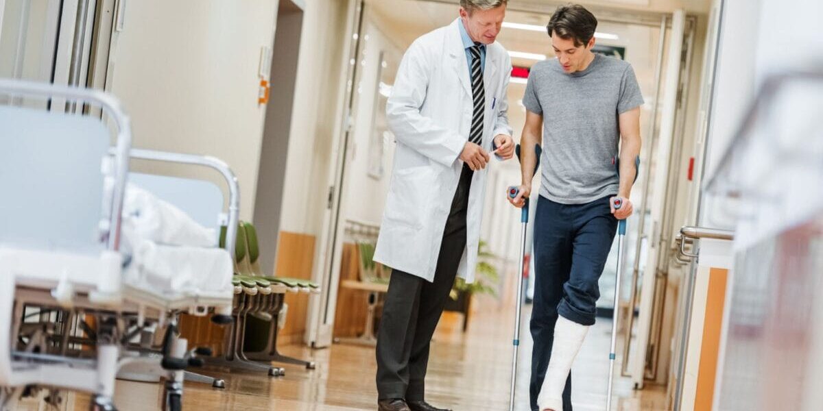 patient-on-crutches a patient walking on crutches alongside a doctor in a country that offers universal healthcare