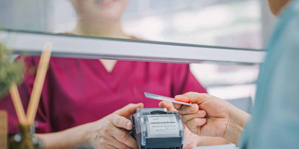 paying-hospital-bill a woman paying a medical bill with a credit card, while a nurse holds the credit card reader in a hospital.