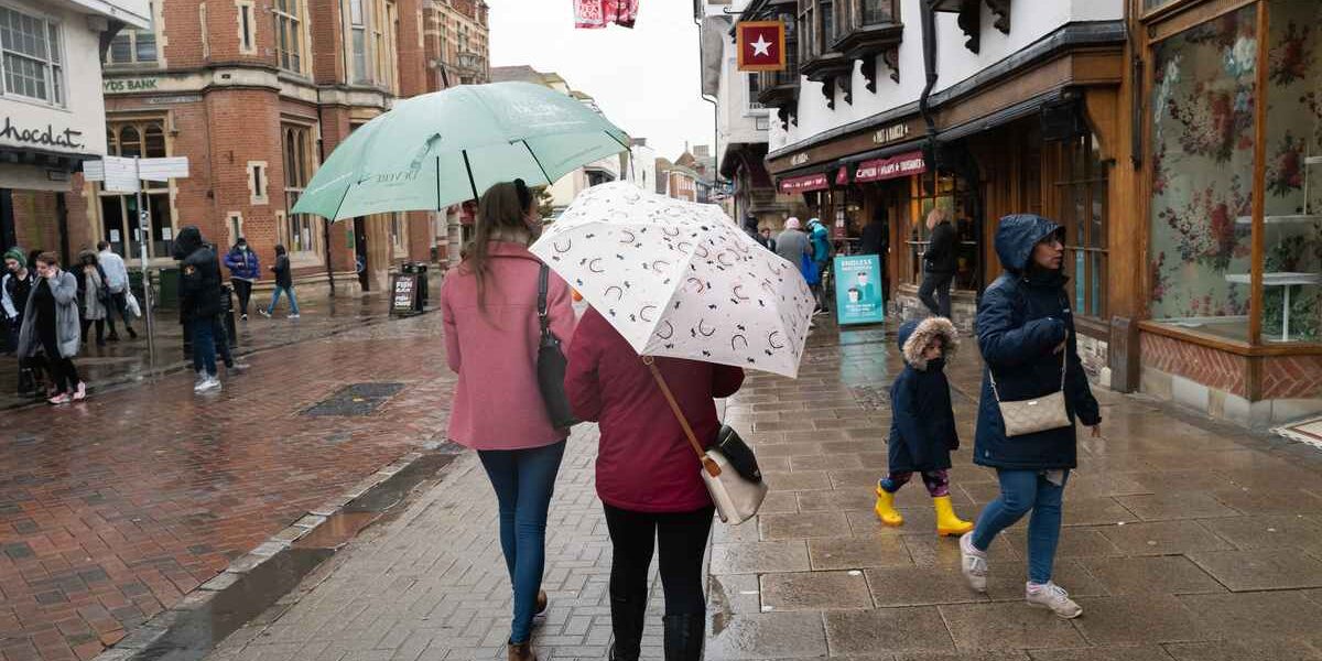shoppers-with-umbrellas two shoppers walking along a UK high street with umbrellas on a rainy day
